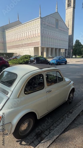 Classic Car at Modern Cathedral: A vintage cream-colored car parked on a paved surface, with a contemporary cathedral featuring a tall bell tower and intricate facade in the background.
