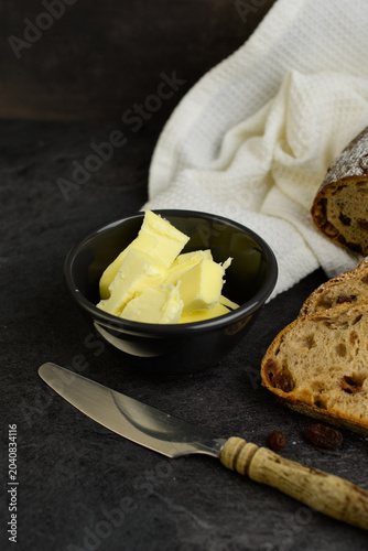 Raisin walnut bread served with butter and fresh blackberries, a bowl of butter and vintage knife on a dark background, rustic breakfast