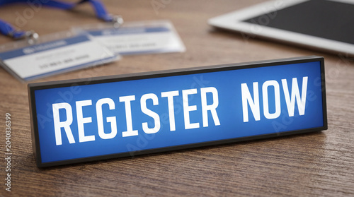 Register now sign at an event desk with id badges and tablet, inviting participants for conference or seminar
