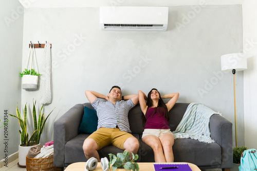 Relaxed couple sitting at home with air conditioning on hot summer day, enjoying cool air and comfort