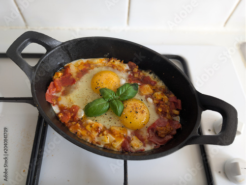 Cast Iron Skillet Breakfast with Sunny Side Eggs Cheddar Chorizo and Basil. Rustic Shakshuka with Eggs in Cast Iron Pan. Overhead view of a traditional Middle Eastern breakfast served on a stovetop