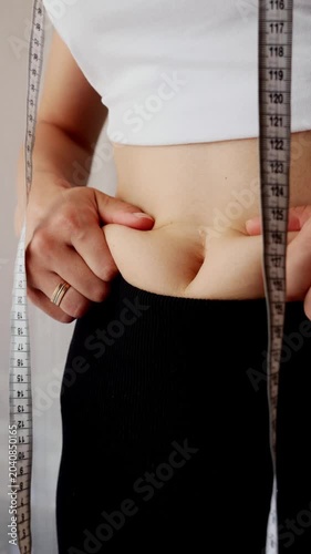 Woman pinching belly fat with Measuring tape, weight loss and body transformation concept.