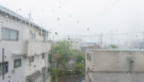 雨の日の窓ガラスについた水滴とぼけた住宅街の背景