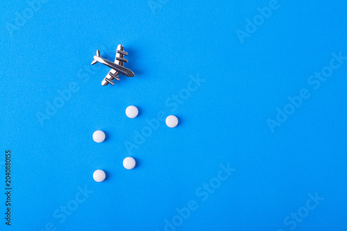 Small plane and pills on blue background. Concept of travel sickness and medicine for the flight. Flat lay with copy space
