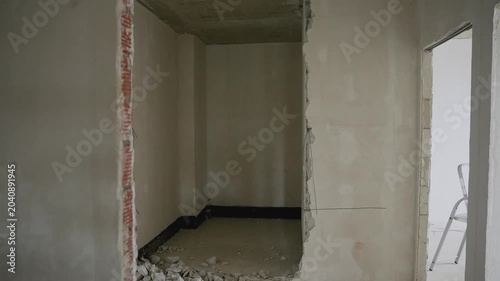 Video captures interior renovation progress as camera zooms out to reveal demolished wall opening with rubble piles and exposed brick edges in unfinished room