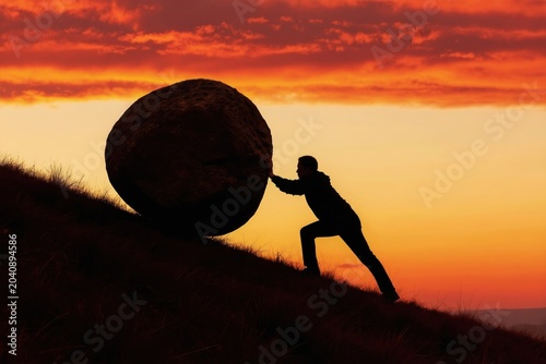 Person silhouette pushes large boulder uphill against dramatic sunset. Represents effort, struggle, and perseverance towards a challenging goal.