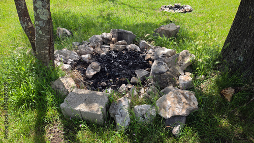 Schilderij op canvas Stone campfire ring with black charcoal ashes on a green grassy lawn