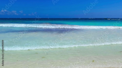 Travel footage, tropical ocean with the blue sky. Waves, white sand and sunny day. Paradise coastline. Turquoise sea. Waves in the water, sandy white beach.