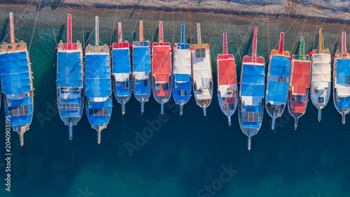 Slika na platnu An aerial drone shot taken from a bird's-eye view showing colorful tour boats lined up side by side in the harbor against the backdrop of the crystal-clear turquoise sea