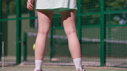 Close-up on the legs of a female athlete serving. A sporty woman hits the padel ball with her racket on an outdoor court
