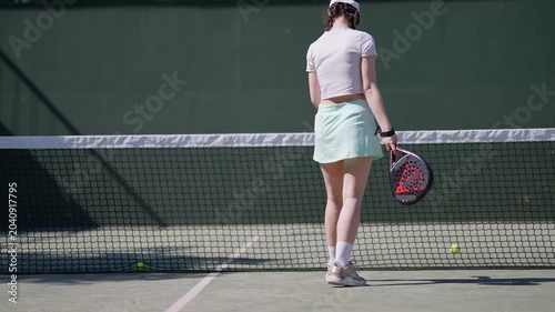 Slow motion footage of a beautiful female player serving the ball with a padel racket. The athlete is training under the sun