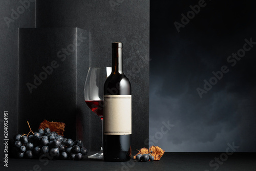 Red wine and blue grapes with dried up vine leaves on a black background.