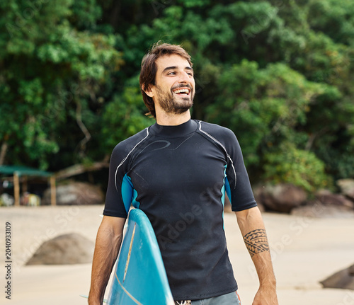 Photography Portrait of a young man surfing at the beach, holding surfboard, ocean waves, he