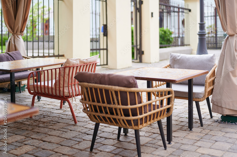 Fototapeta premium Outdoor cafe with wicker chairs and tables on a stone floor. Cozy terrace for relaxing and eating.