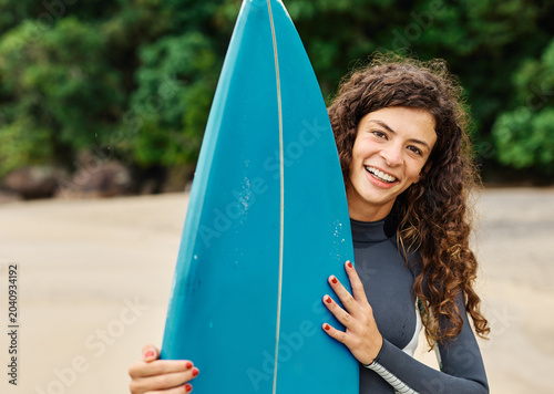Photography Portrait of a young woman surfing at the beach, holding surfboard, ocean waves,
