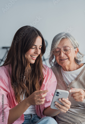 Fotografie Young woman helping an older woman understand and use a smartphone, bridging a g