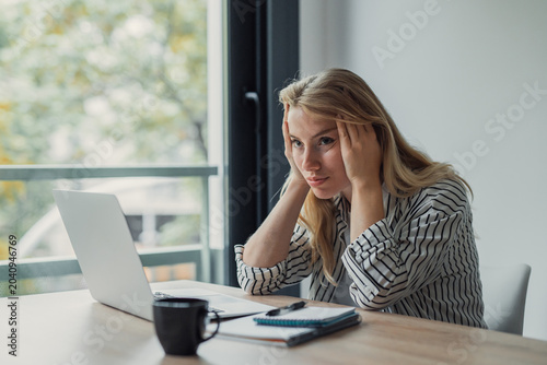 Foto Stressed young professional woman holding her head at a home office desk, fatigu