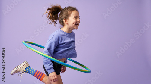 Happy Young Girl Running with Hula Hoop on Purple Background