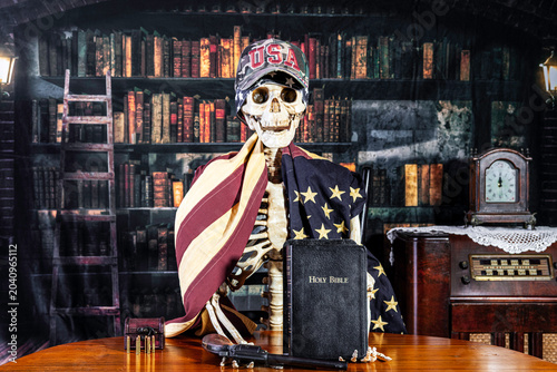 Canvas-taulu Skeleton draped with American flag clinging to his gun and bible with old librar