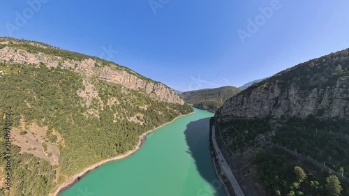 Aerial low altitude flight, pilot view, in a narrow valley over alpine lake with Alpine mountain reflections on calm water, Provence, France