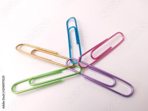 Five colorful paper clips—blue, pink, purple, green, and gold—are arranged overlapping in a circular, star-like pattern