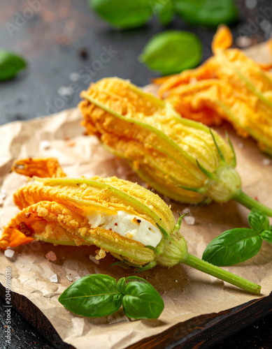 Delicate zucchini blossoms stuffed with ricotta cheese and deep fried until golden on a rustic paper-lined wooden board.