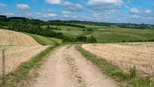 Countryside path winding along a harvested stubble field towards a stone church
