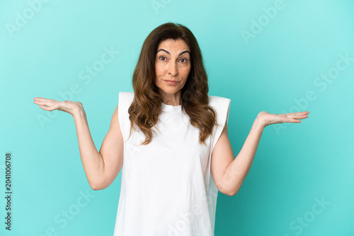 Billede på lærred Middle aged caucasian woman isolated on blue background having doubts while rais
