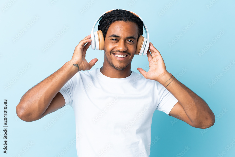 Naklejka premium Young African American man with braids isolated on blue background listening music