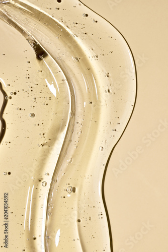 Transparent gel, serum, or oil spreading on a neutral background, showing a liquid texture with bubbles