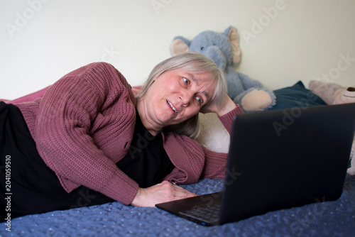 Mature woman smiling softly while watching laptop during video call at home