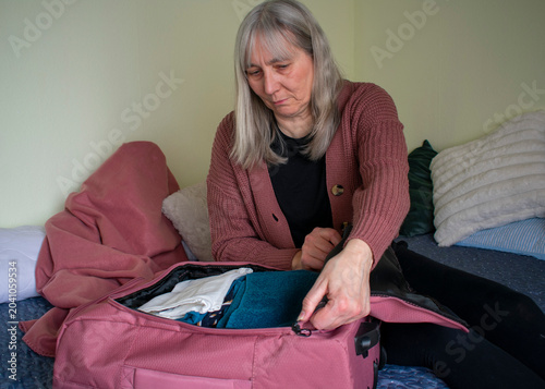 Close up of senior woman closing suitcase zipper while packing