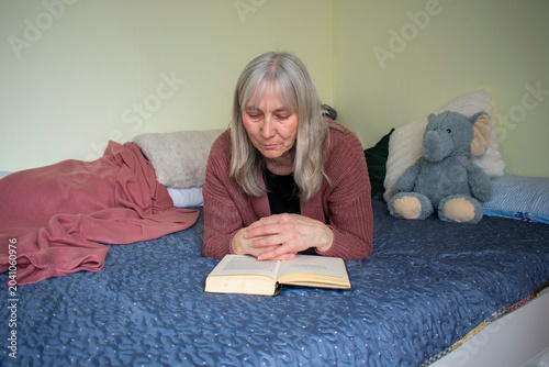 Senior woman reading a book while lying on bed in a calm home environment
