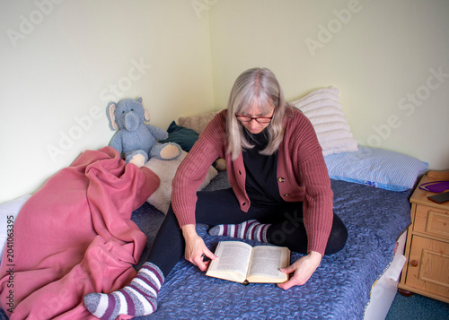 Senior woman sitting on bed reading a book in a quiet moment at home