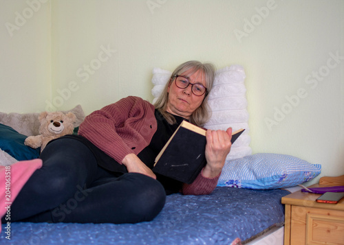 Senior woman lying on bed reading a book in a quiet and peaceful moment at home