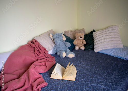 Open book on bed with pillows and stuffed toys in cozy bedroom interior