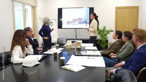 Two diverse female architects delivering a presentation on a new architectural project to a group of colleagues in a modern office boardroom