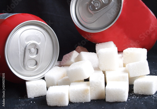 Unhealthy diet concept: A large pile of white sugar cubes next to generic red soda cans representing high calorie and sugar content in soft drinks