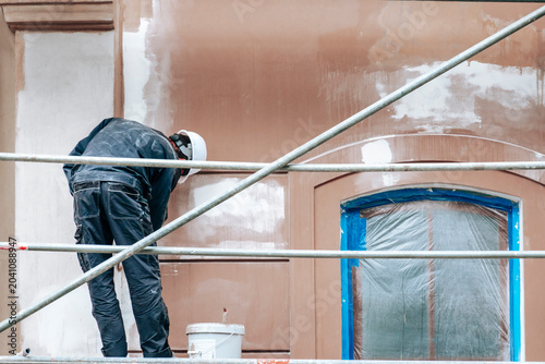 Obraz na płótnie Unrecognizable construction worker standing on scaffolding and renovating buildi