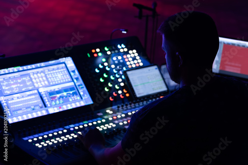 Foto Male sound engineer operating a digital mixing console with illuminated controls
