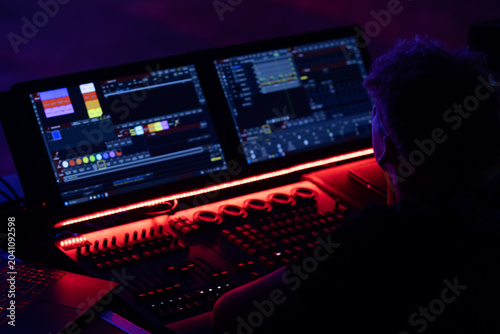 Individual operating lighting control console with multiple screens displaying colorful graphics and controls in a darkened environment with ambient lighting
