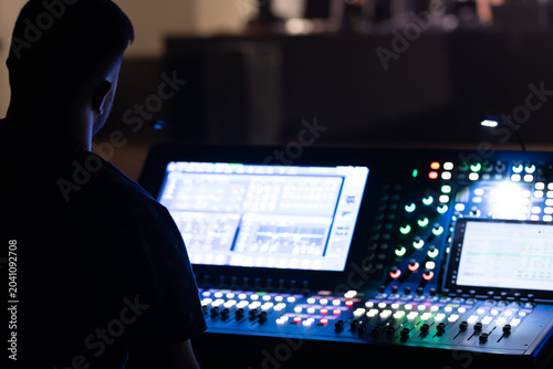 Obraz na plátně Sound technician operating a digital audio mixer with illuminated controls in a