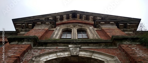 A striking low-angle view of a grand, historic brick building featuring intricate architectural details and a majestic rooftop against a cloudy sky, exuding timeless elegance.