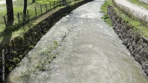 Fast flowing muddy river water in a stone canal during spring