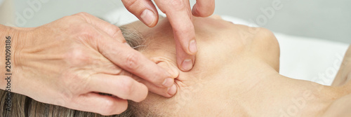Photos Therapist Applying Acupressure To Temple And Jaw Of Reclining Adult Patient On Treatment Table In Wellness Clinic During Manual Therapy Session With Gentle Fingertip Pressure For Muscle Release