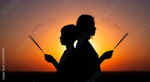 Silhouetted Couple Holding Incense Sticks Back to Back at Sunset