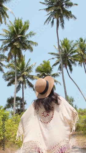 Pretty woman in pink shorts and straw hat walking to beach enjoy relaxation on tropical island. Lush palm trees and sunny path in Southeast Asia. Summer vacation get away holidays solo travel.