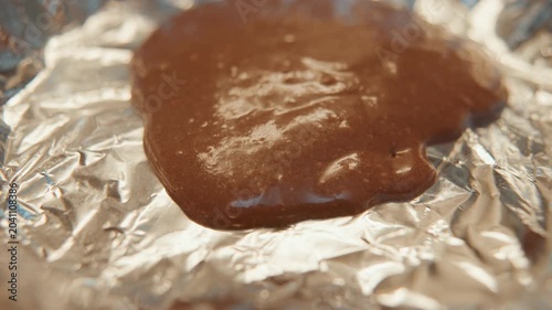 Closeup chocolate batter on foil, glossy brown mixture resting on crinkled aluminum, thick texture catching warm kitchen light, evokes homemade dessert preparation and tactile richness