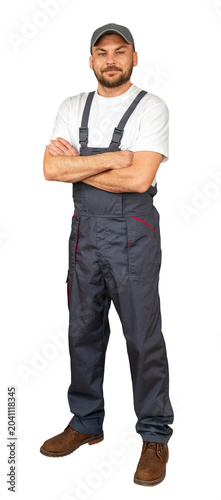 Handyman with crossed arms posing in grey bib overalls and cap.