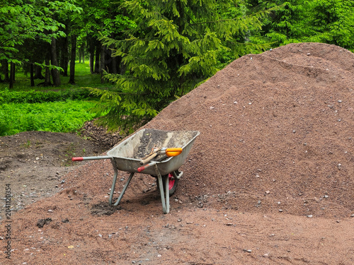 Close up metal wheelbarrow rests beside a pile of crushed red mulch.